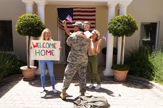 Caucasian boy hugging father in military uniform with family standing at entrance of house. family, love and patriotism concept, unaltered.