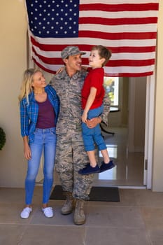 Happy caucasian family with army soldier standing at the entrance of house with usa flag. family, love and patriotism concept, unaltered.