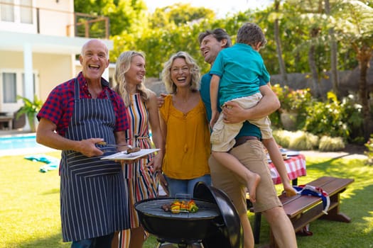 Portrait of cheerful caucasian three generational family barbecuing together in the garden. family, togetherness and weekend lifestyle concept, unaltered.