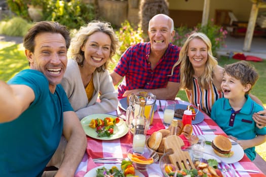 Portrait of cheerful caucasian family taking selfie at table in the garden. family, togetherness and weekend lifestyle concept, unaltered.