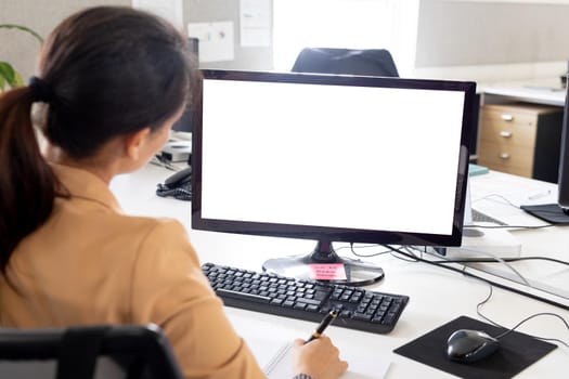 Rear view of businesswoman working on computer monitor at desk in office, copy space. unaltered, creative business, advertisement and technology concept.