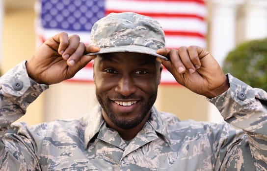 Portrait of smiling male african american army soldier wearing cap and uniform against flag. identity and patriotism, unaltered.