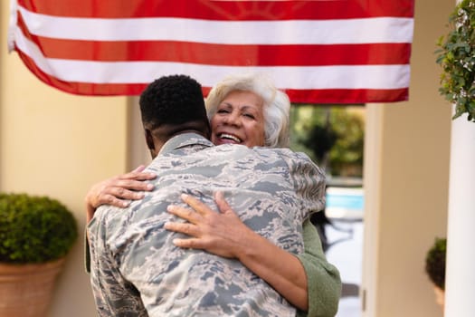 Happy senior african american woman embracing soldier son on his return home at entrance. family, bonding and patriotism, unaltered.
