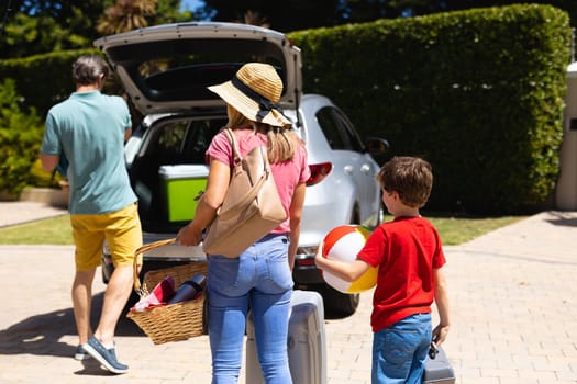 Happy caucasian family putting their luggage in their car on sunny day. family trip and vacation concept, unaltered.