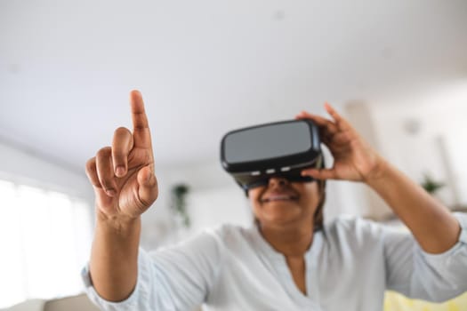African american senior woman pointing while wearing virtual reality simulator at home, copy space. lifestyle, futuristic and modern technology.