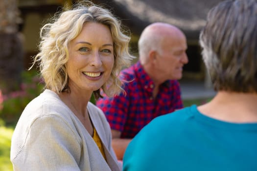 Portrait of blond senior caucasian woman sitting with family in the garden. family, togetherness and weekend lifestyle concept, unaltered.