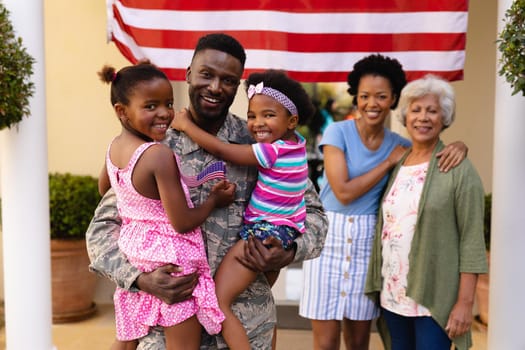 Portrait of smiling african american family with military soldier standing at house entrance. bonding and patriotism, unaltered.