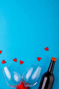 Red heart shapes by wine bottle and empty wineglasses over blue background with copy space. love and valentine celebration.