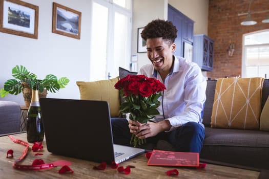 Happy young man holding fresh red rose bouquet during virtual date through laptop at home. lifestyle, virtuality and telecommunications.