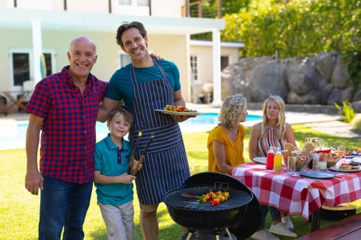 Portrait of caucasian grandfather, father and son barbecuing in the garden. family, love and togetherness concept, unaltered.