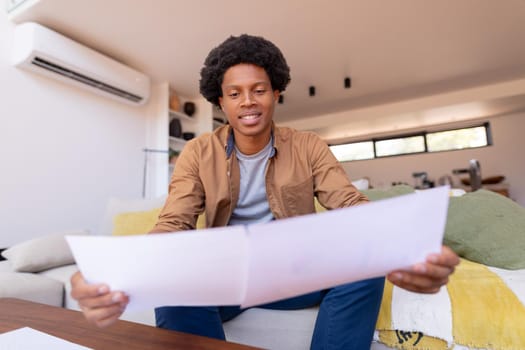 Smiling african american young businessman reading documents while working at home. unaltered, business, working at home concept.