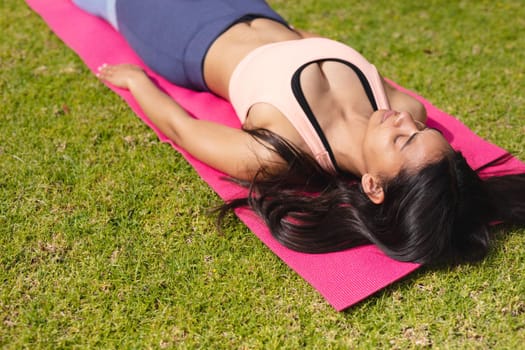 Young woman in sportswear practicing shavasana on exercise mat in park. yoga, healthy lifestyle and body care.