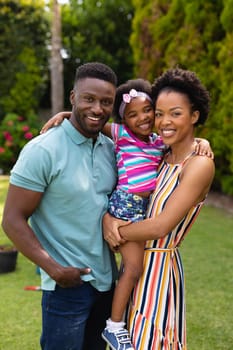 Portrait of smiling african american parents carrying daughter at garden. family, love and togetherness concept, unaltered.