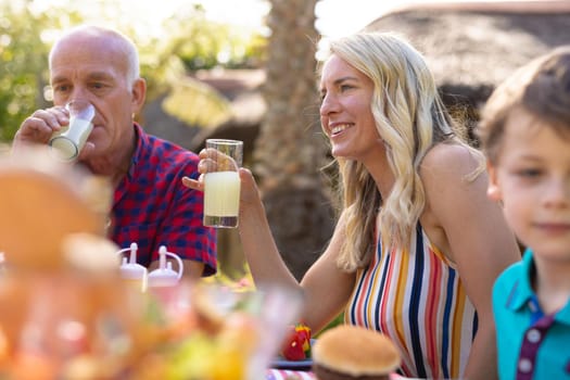 Smiling caucasian woman holding drink sitting together with family in the garden. family, togetherness and weekend lifestyle concept, unaltered.