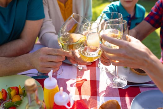 Midsection of caucasian family toasting drinks at table in garden. family, togetherness and weekend lifestyle concept, unaltered.