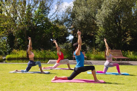 Men and women with arms raised practicing yoga on exercise mats in park on sunny day. healthy lifestyle and body care.