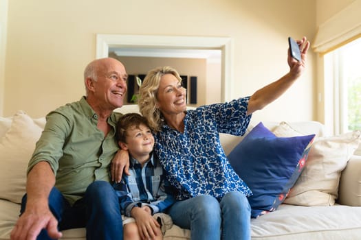 Caucasian grandparents and grandson taking a selfie while sitting together on couch at home. family, love and togetherness concept, unaltered.