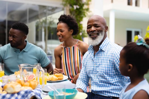 Portrait of smiling senior african american man sitting with family at backyard during brunch. family, love and togetherness concept, unaltered.