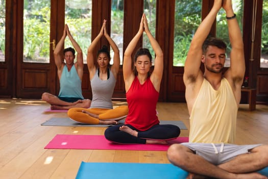 Men and women sitting with cross-legged and hands clasped meditating at health club. healthy lifestyle, fitness and yoga.