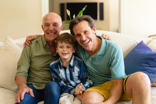 Portrait of caucasian grandfather, father and son smiling while sitting together on couch at home. family, love and togetherness concept, unaltered.
