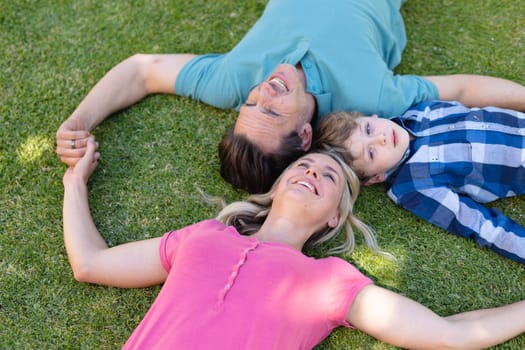 High angle view of smiling caucasian family holding hands and lying together in the garden. family, love and togetherness concept, unaltered.
