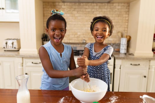 Portrait of happy two african american sisters baking together in the kitchen at home. family, love and togetherness concept, unaltered.
