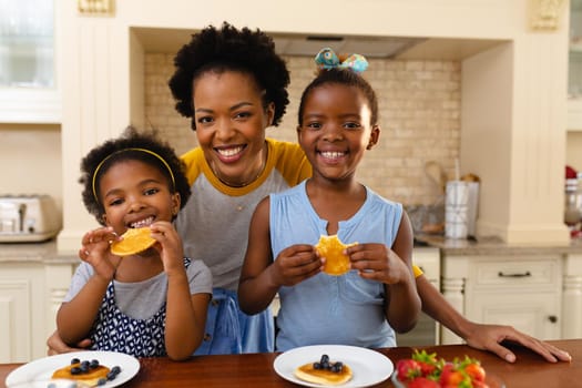 Portrait of african american mother and her two daughters having breakfast in kitchen at home. family, love and togetherness concept, unaltered.