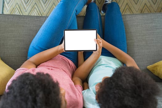 Teenage girl teaching mother to use digital tablet while sitting on sofa at home, copy space. wireless technology, lifestyle, family and advertising concept.