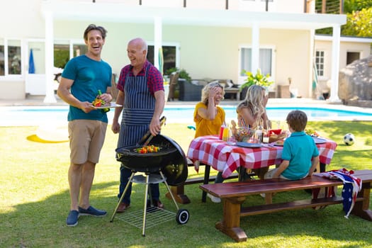 Caucasian father and son laughing while barbecuing in the garden. family, love and togetherness concept, unaltered.