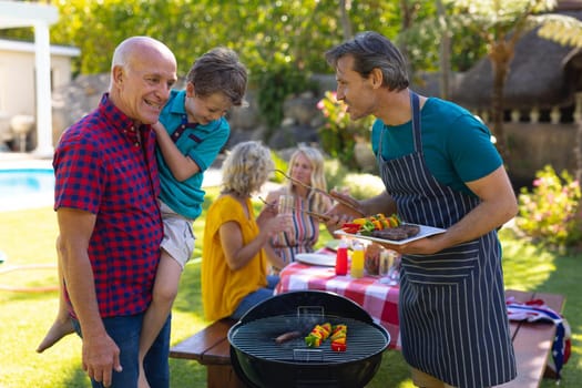 Caucasian grandfather, father and son barbecuing meal together in garden. family, togetherness and weekend lifestyle concept, unaltered.