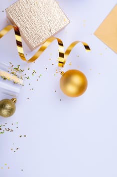 Golden ribbon and baubles by gift box and champagne flute with confetti on white background. christmas celebration and party decoration with copy space.
