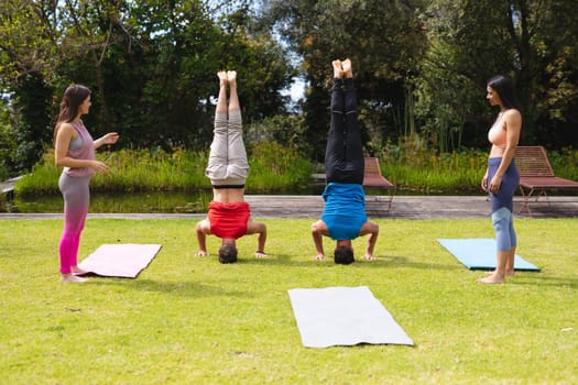 Full length of women looking at men practicing handstand in park on sunny day. yoga, healthy lifestyle and body care.