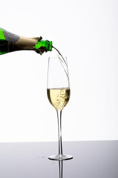 Closeup of bottle pouring champagne in flute on table against white background with copy space. celebratory party drink.
