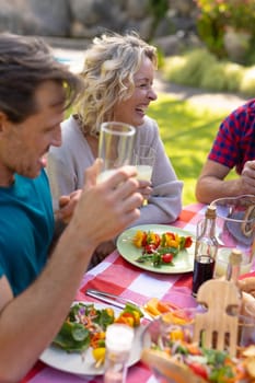 Cheerful caucasian senior woman sitting with family sitting together in garden during lunch. family, togetherness and weekend lifestyle concept, unaltered.