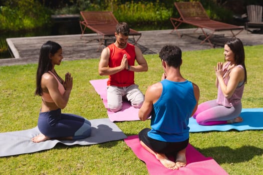 Men and women meditating on exercise mats in public park on sunny day. yoga, healthy lifestyle and body care.