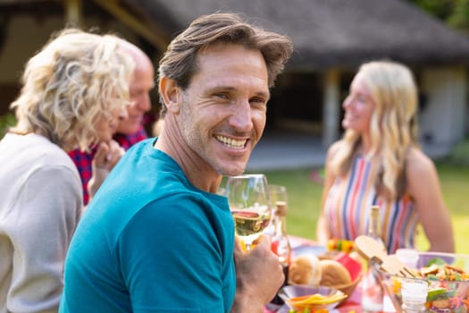 Portrait of smiling caucasian man sitting together with family at table in garden. family, togetherness and weekend lifestyle concept, unaltered.