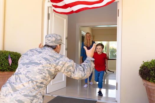 Caucasian mid adult woman looking at caucasian son running to mid adult male soldier at doorway. unaltered, family, greeting, us military, happiness and homecoming.