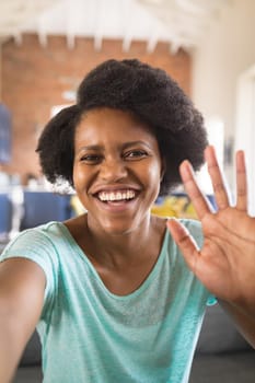 Portrait of happy african american woman waving hand on video call at home. influencer, communication and vlogging concept.
