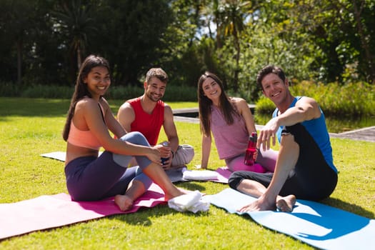 Portrait of smiling men and women sitting on exercise mats after workout in park. yoga, healthy lifestyle and friendship.