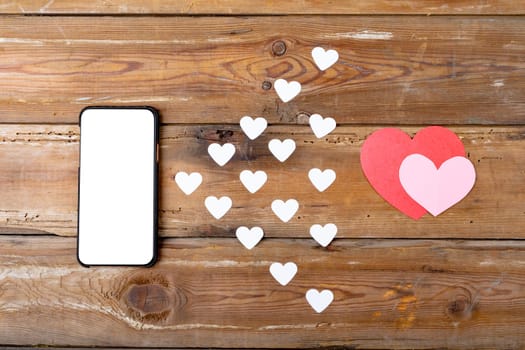 Overhead view of blank screen on smart phone by heart shaped decoration on table, copy space. valentine's day, wireless technology and love concept.