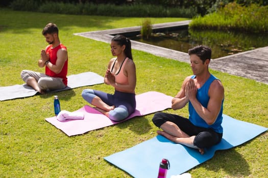 Men and woman in sportswear sitting with hands clasped while meditating on exercise mats in park. yoga, healthy lifestyle and body care.
