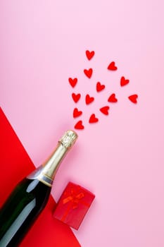 Champagne bottle splashing red heart shapes by gift box on pink background. love, gift and valentine celebration with copy space.