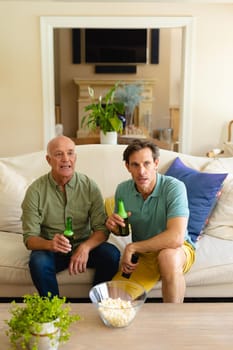 Caucasian father and son with beer watching tv together on the couch at home. sports and entertainment concept, unaltered.