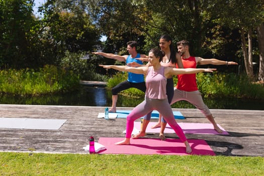 Female yoga instructor assisting woman and men in exercising at park. healthy lifestyle and body care.