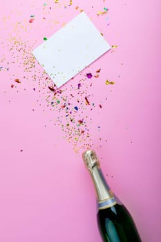 Overhead view of champagne bottle with scattered confetti with copy space on blank paper. celebration and party message.