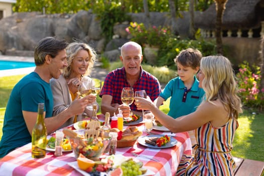 Happy caucasian family toasting drinks while sitting together at table in garden. family, togetherness and weekend lifestyle concept, unaltered.