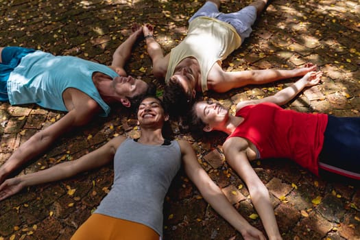 Smiling multiracial male and female friends relaxing together with arms outstretched on ground. yoga, healthy lifestyle and fitness.