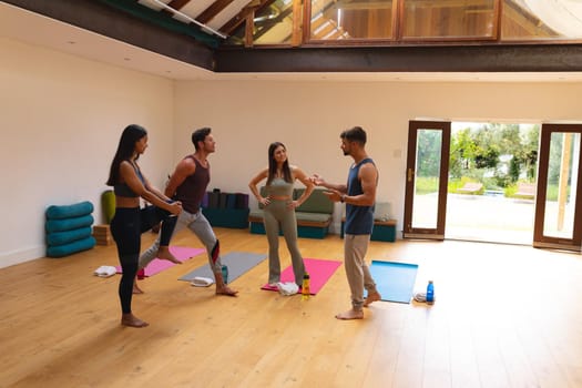 Multiracial male and female friends talking while doing warm up exercise in yoga studio. fitness, yoga and healthy lifestyle.