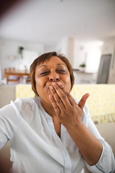 Happy african american senior woman blowing kiss during video call at home. lifestyle and communication.