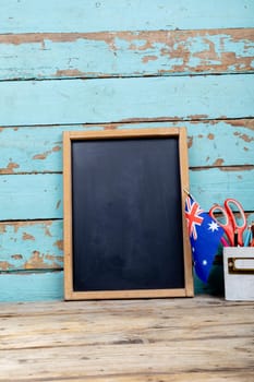 Blank writing slate by australia flag and desk organizer against blue wooden wall with copy space. independence day, national flag and patriotism.